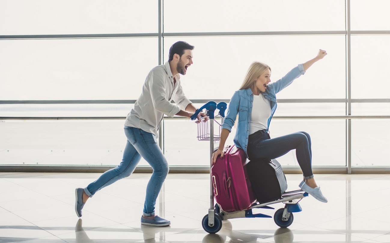 Romantic couple in airport. Attractive young woman and handsome man with suitcases are ready for traveling. Having fun on luggage trolley while waiting for departure.; Shutterstock ID 1033801798; your: Ben N Buckner; gl: 65050; netsuite: Online Editorial; full: Seven Corners Sponsored