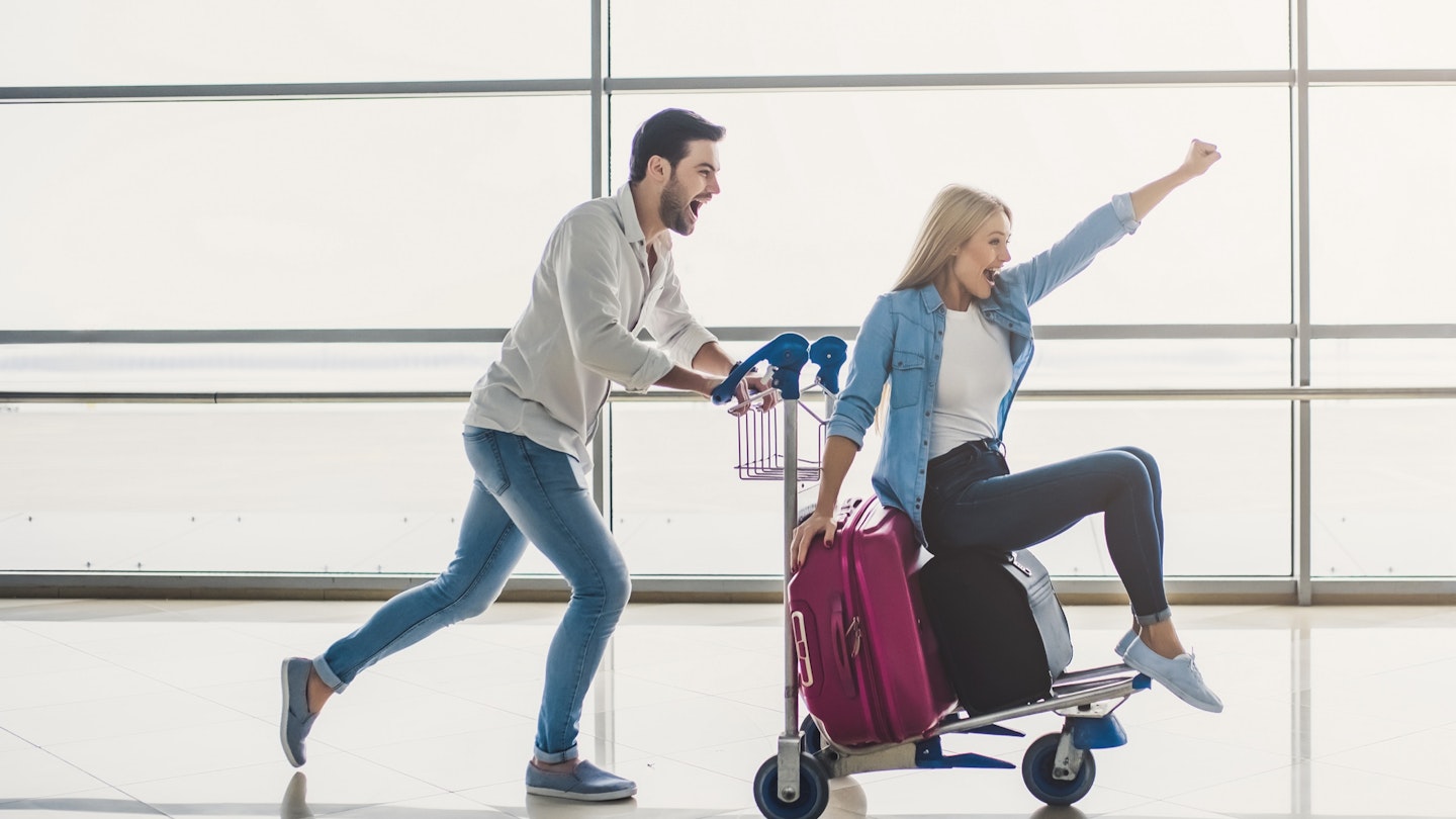 Romantic couple in airport. Attractive young woman and handsome man with suitcases are ready for traveling. Having fun on luggage trolley while waiting for departure.; Shutterstock ID 1033801798; your: Ben N Buckner; gl: 65050; netsuite: Online Editorial; full: Seven Corners Sponsored