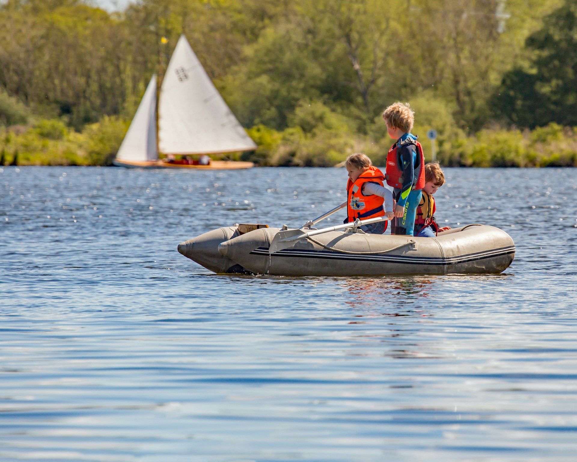 Three young children in a dinghy out on the water observe a fancy yacht sailing by
