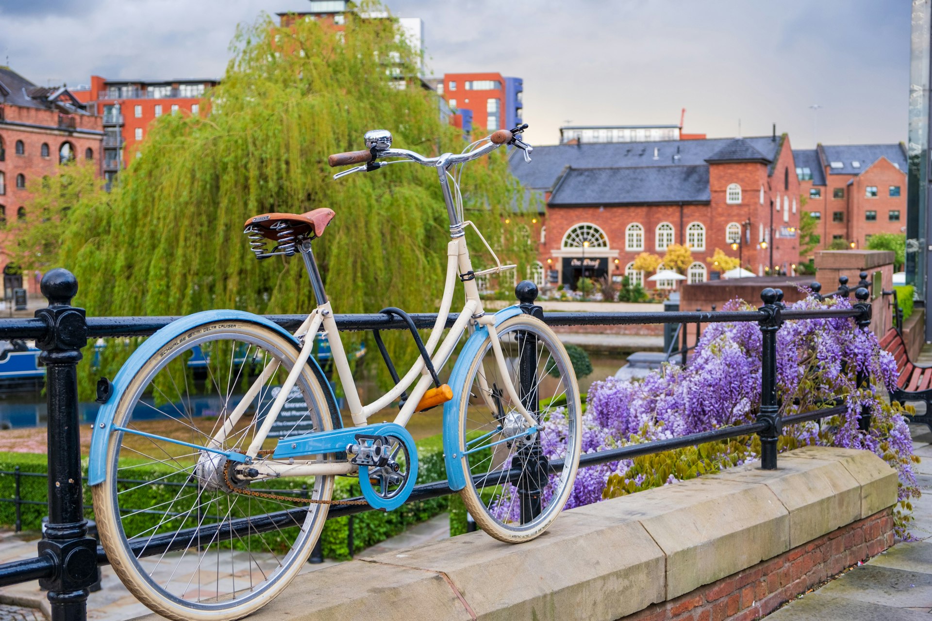 A bicycle parked beside a restored Victorian canal system in the Castlefield area of Manchester. Purple wisteria is flowering on the wall