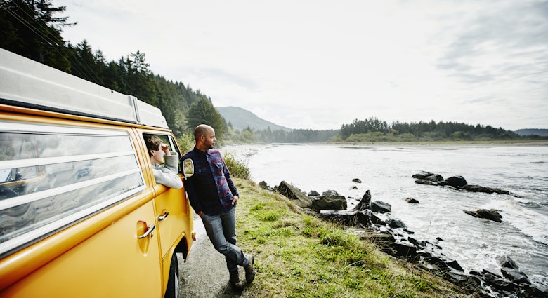 Husband and wife on road trip in van parked on side of road near ocean looking out