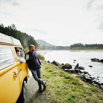 Husband and wife on road trip in van parked on side of road near ocean looking out