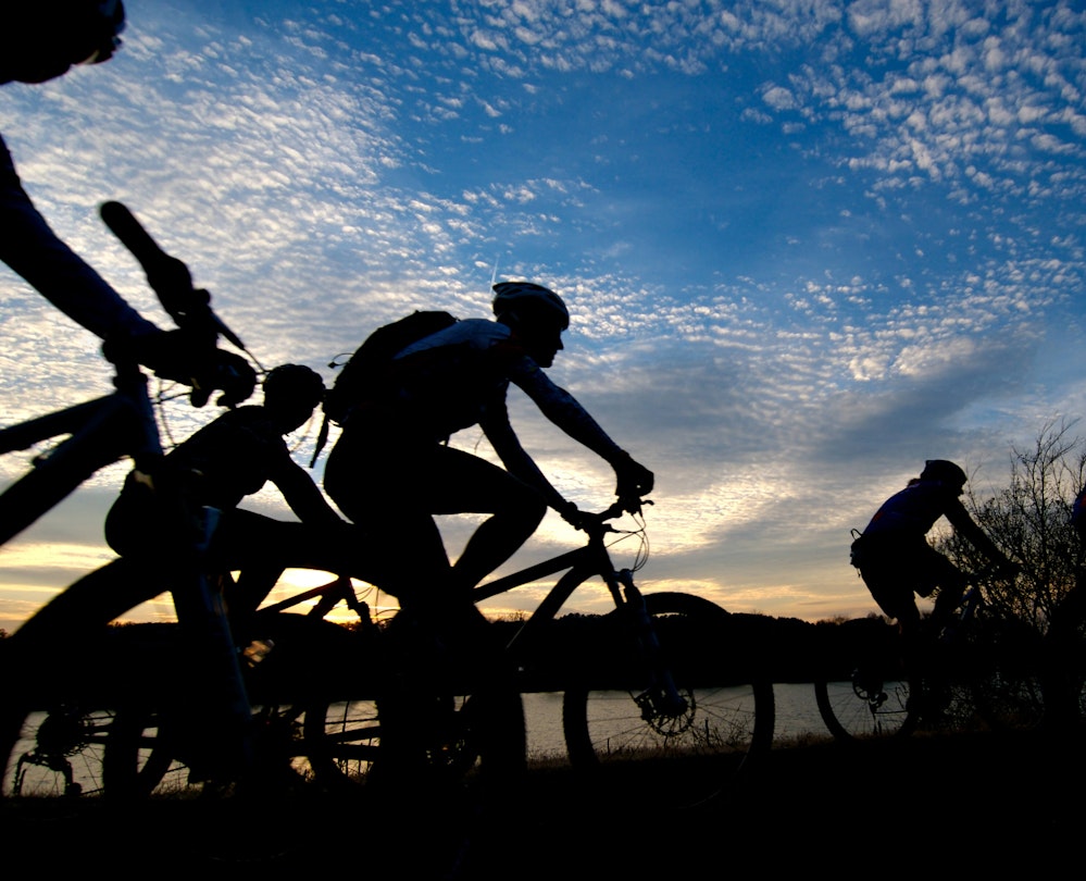 Group of bicyclists rides along the Arkansas River at sunset