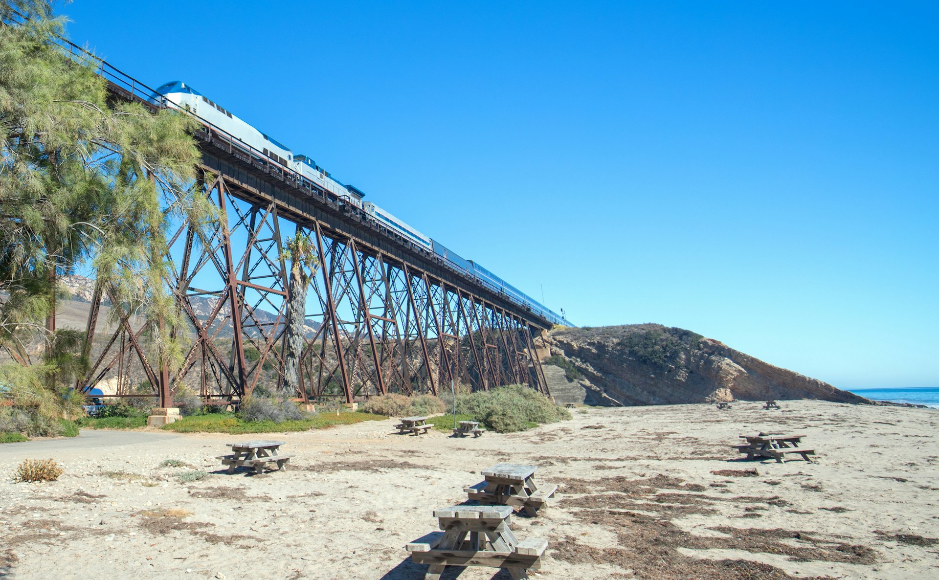 Train traveling over a railroad track bridge that rises high above a beach