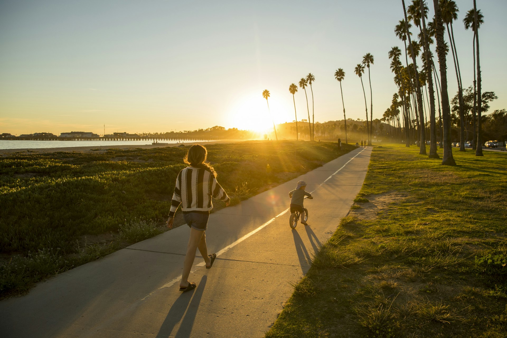 A mother and her son riding a bike along a palm-fringed beachside path in Santa Barbara