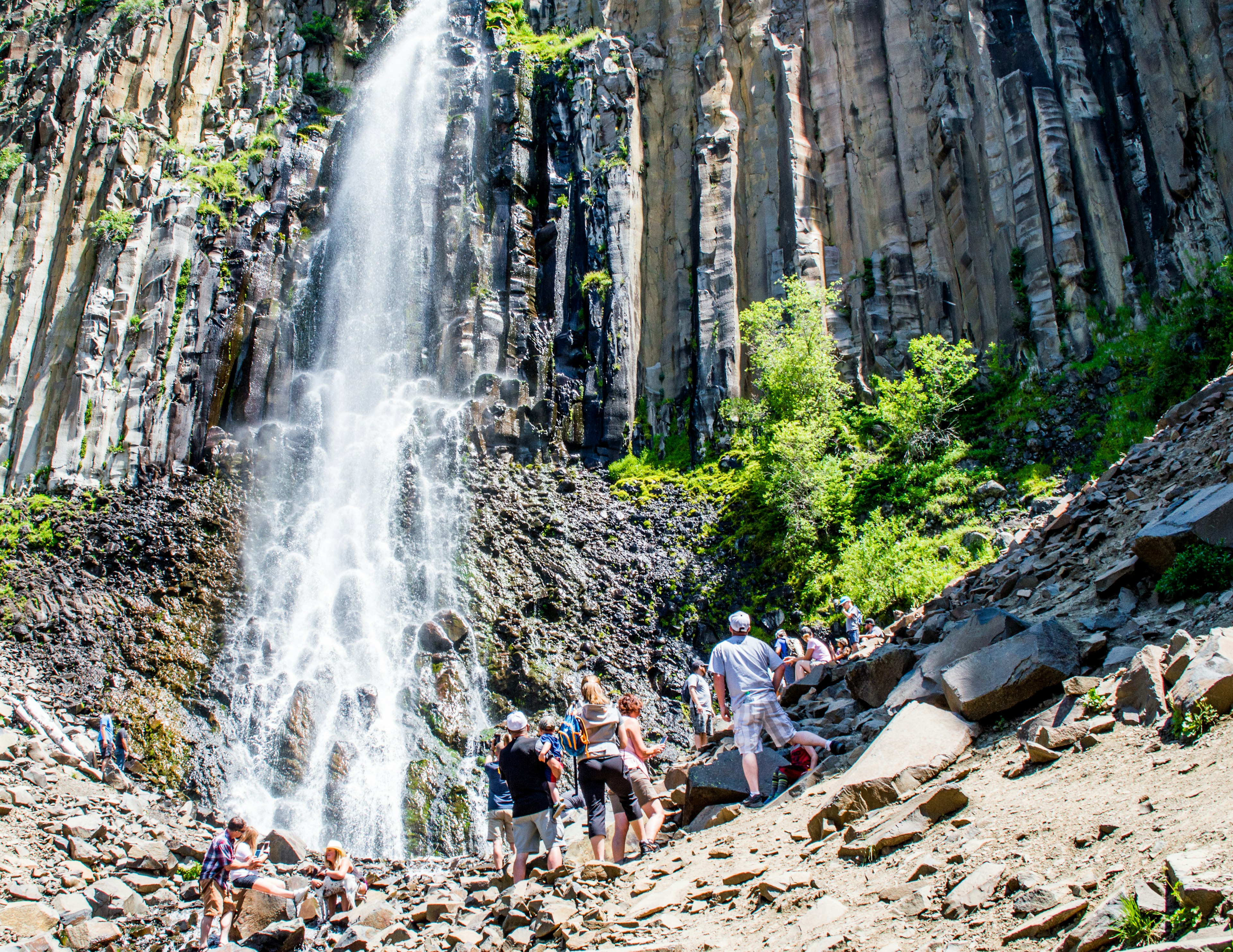 A group of hikers look up at the basalt rock face of Palisade Falls waterfall, near Bozeman, Montana, Rocky Mountains, USA