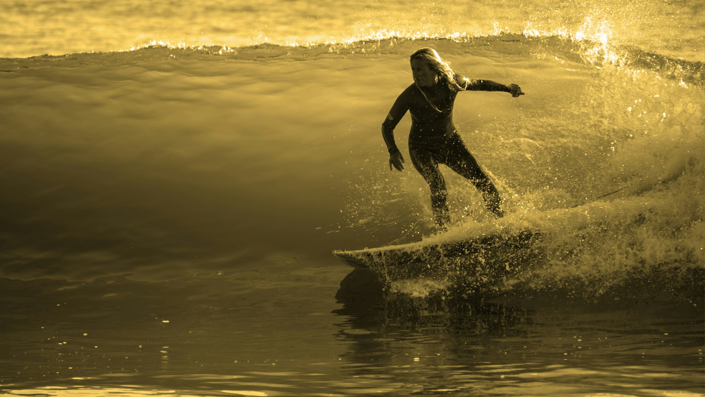 A surfer rides an ocean wave at sunset