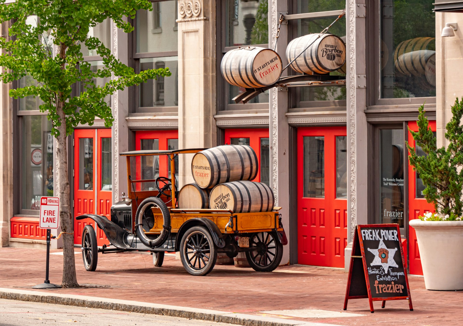 Exterior of the Frazier History Museum in Louisville, KY which includes old barrels of bourbon stacked up atop a 1920s-style open-back truck