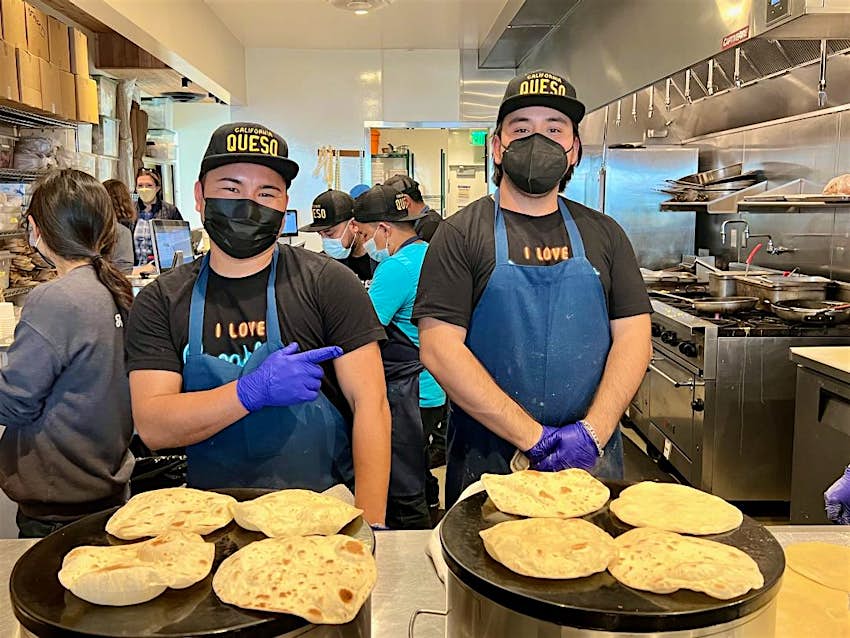 Two people in masks, hats, gloves and aprons making tortillas on comales at HomeState