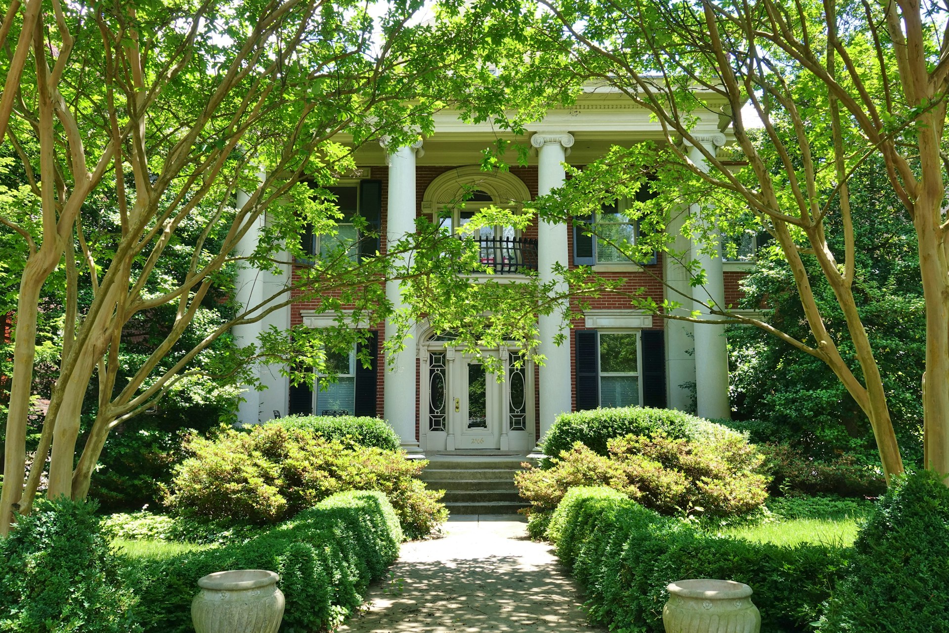 The front of an elegant historic mansion house lined with greenery