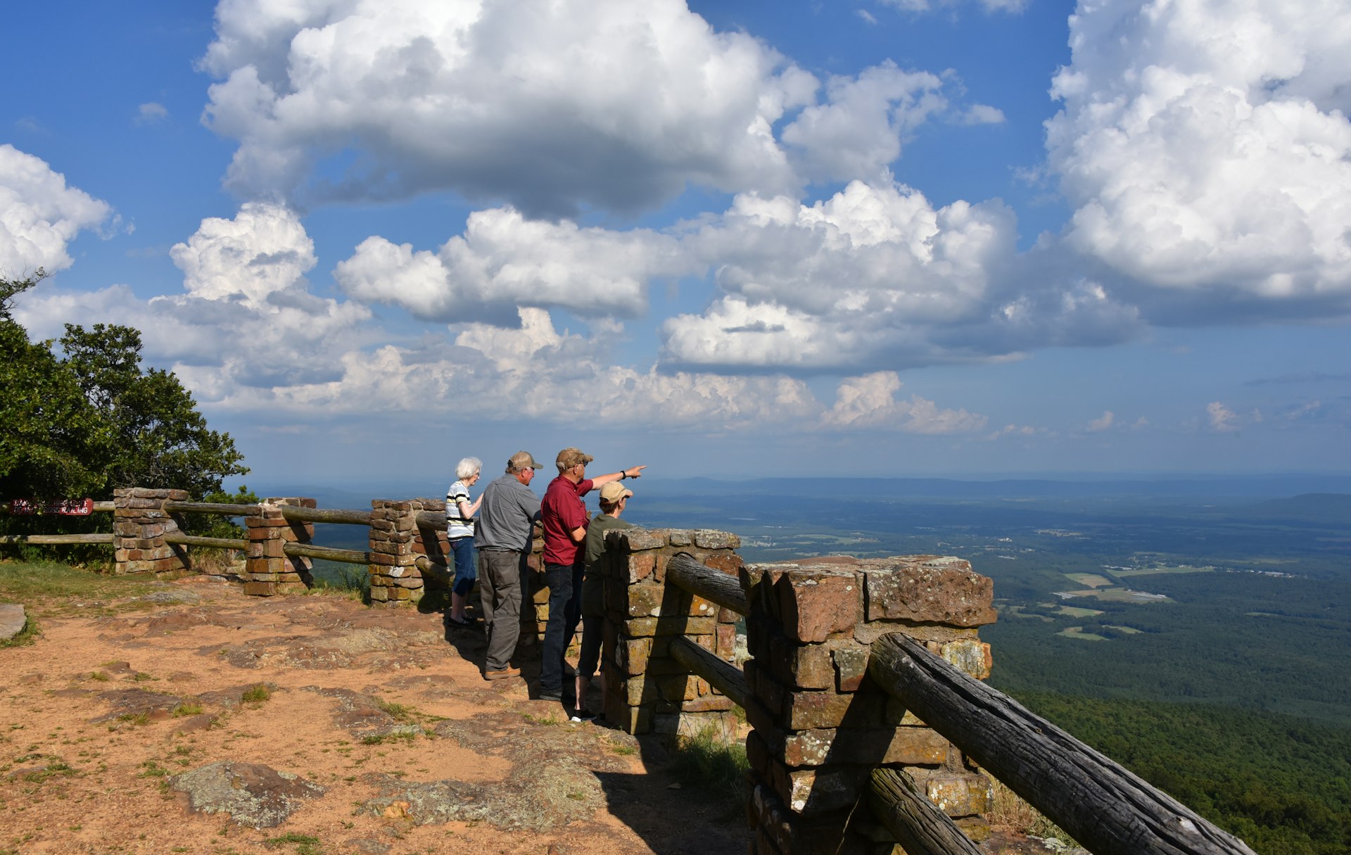 Four people ranging from a child to an older person stand at a mountain viewpoint looking out at rural landscape in the Ozarks, Arkasas