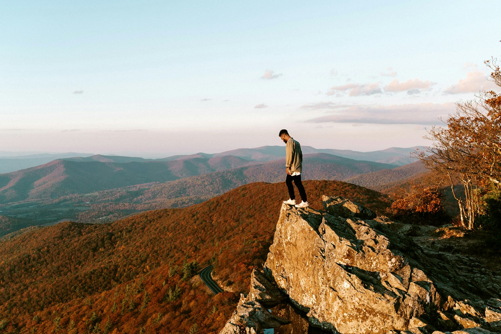 Man stood on the edge of a large rock overlooking the scenic Shenandoah National Park in fall colours