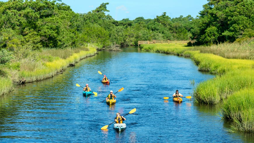 Five people kayaking in Southport on the Brunswick Islands. Blue water and green marshes around. Spring or summer