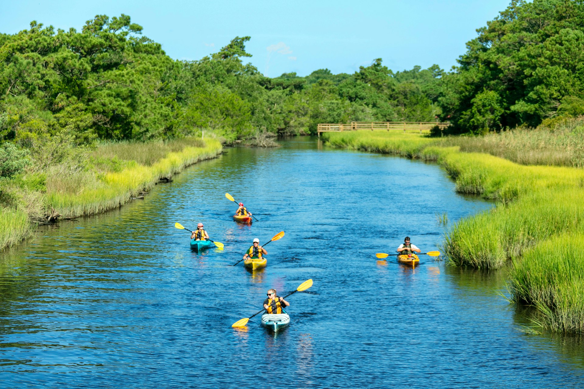Five people kayaking in Southport on the Brunswick Islands. Blue water and green marshes around. Spring or summer