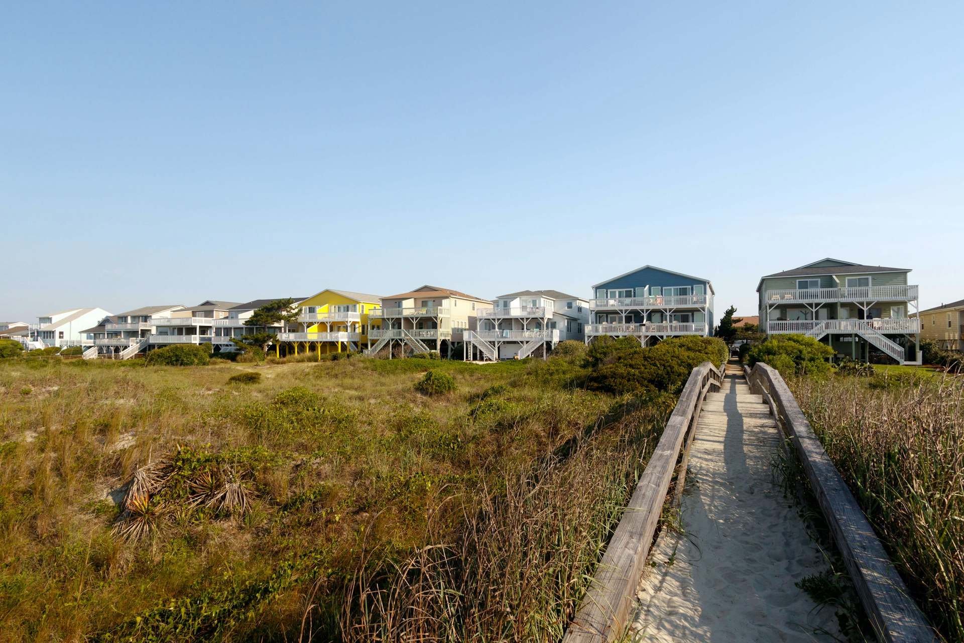 Beach houses across the green sand dunes with a long wooden walkway, Sunset Beach, North Carolina 