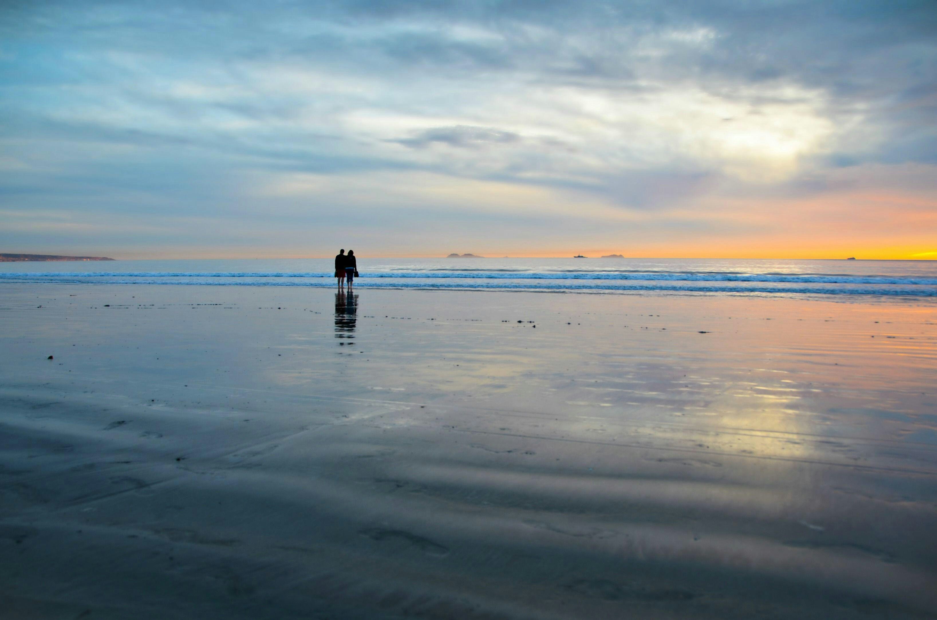 2E5BKXB Young couple silhouettes on the Silver Strand Beach wet sand  watching the sunset at Coronado Island, San Diego Southern California USA.