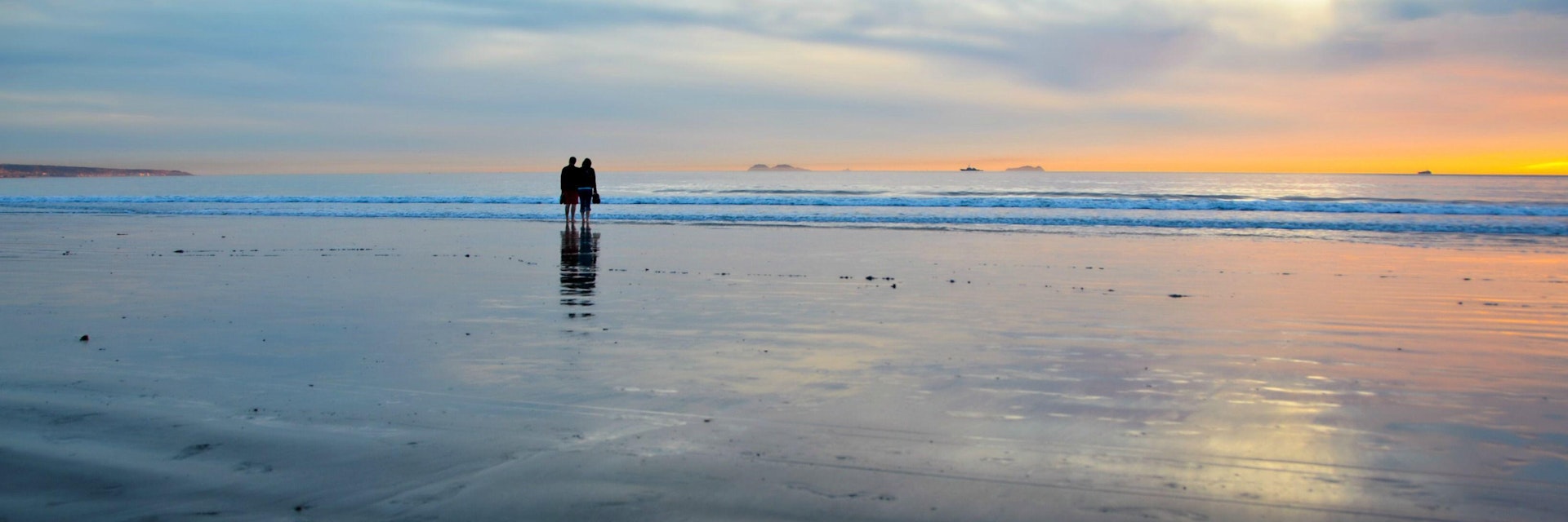 2E5BKXB Young couple silhouettes on the Silver Strand Beach wet sand  watching the sunset at Coronado Island, San Diego Southern California USA.