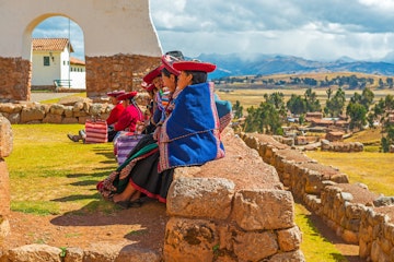 CHINCHEROS, PERU - JUNE 23, 2013: A group of Quechua women sitting on an ancient Inca wall in an archaeological site during a social gathering, all in traditional clothing at sunset near Cusco city.