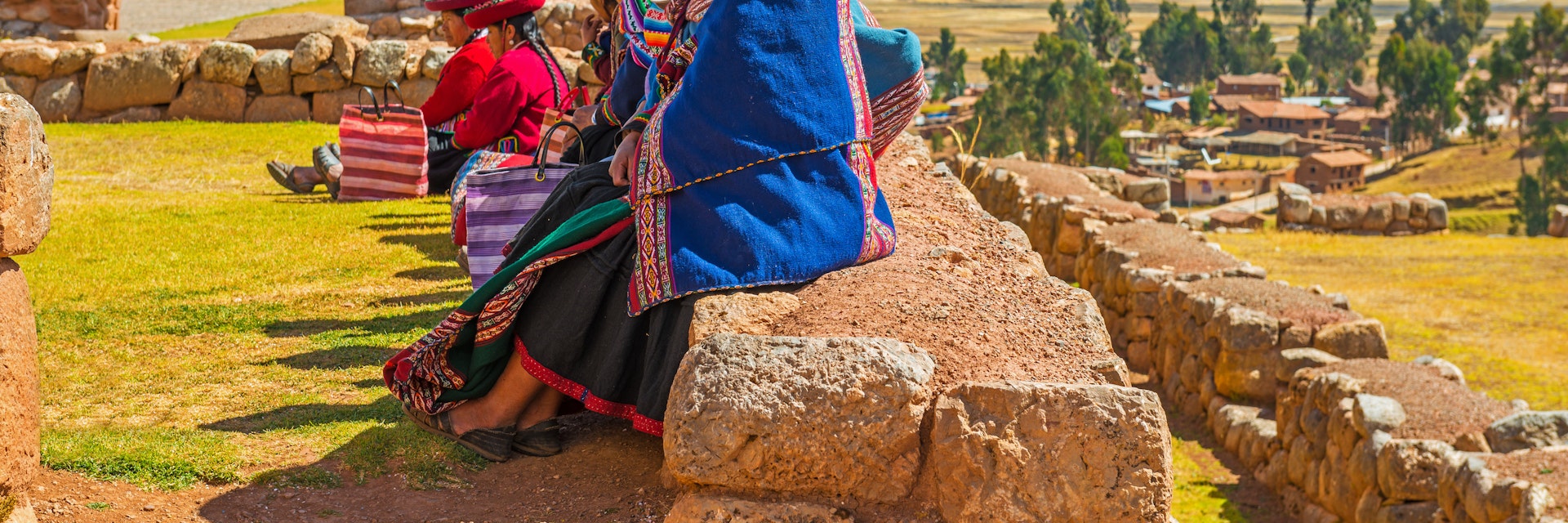 CHINCHEROS, PERU - JUNE 23, 2013: A group of Quechua women sitting on an ancient Inca wall in an archaeological site during a social gathering, all in traditional clothing at sunset near Cusco city.
