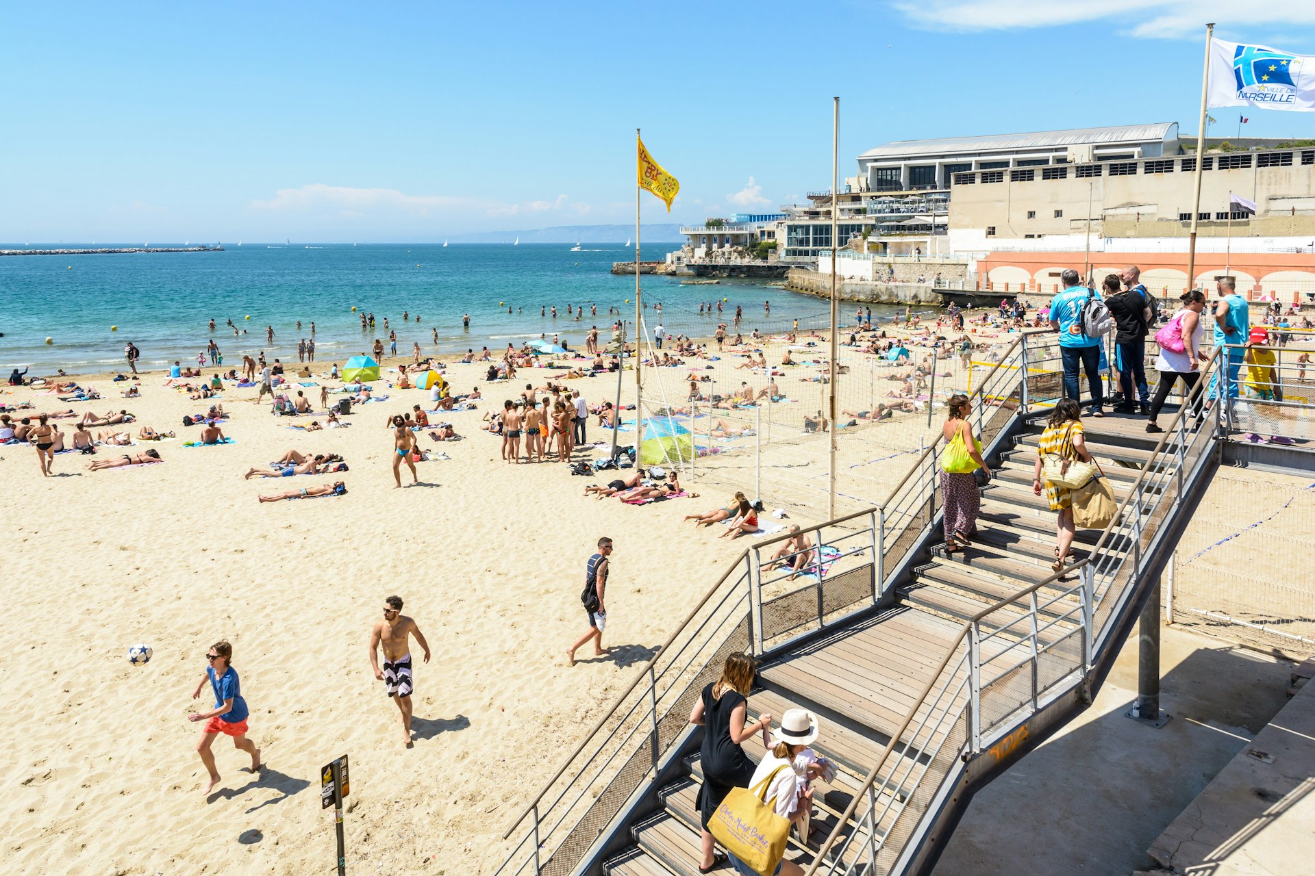 A wooden staircase leading down to a crowded beach