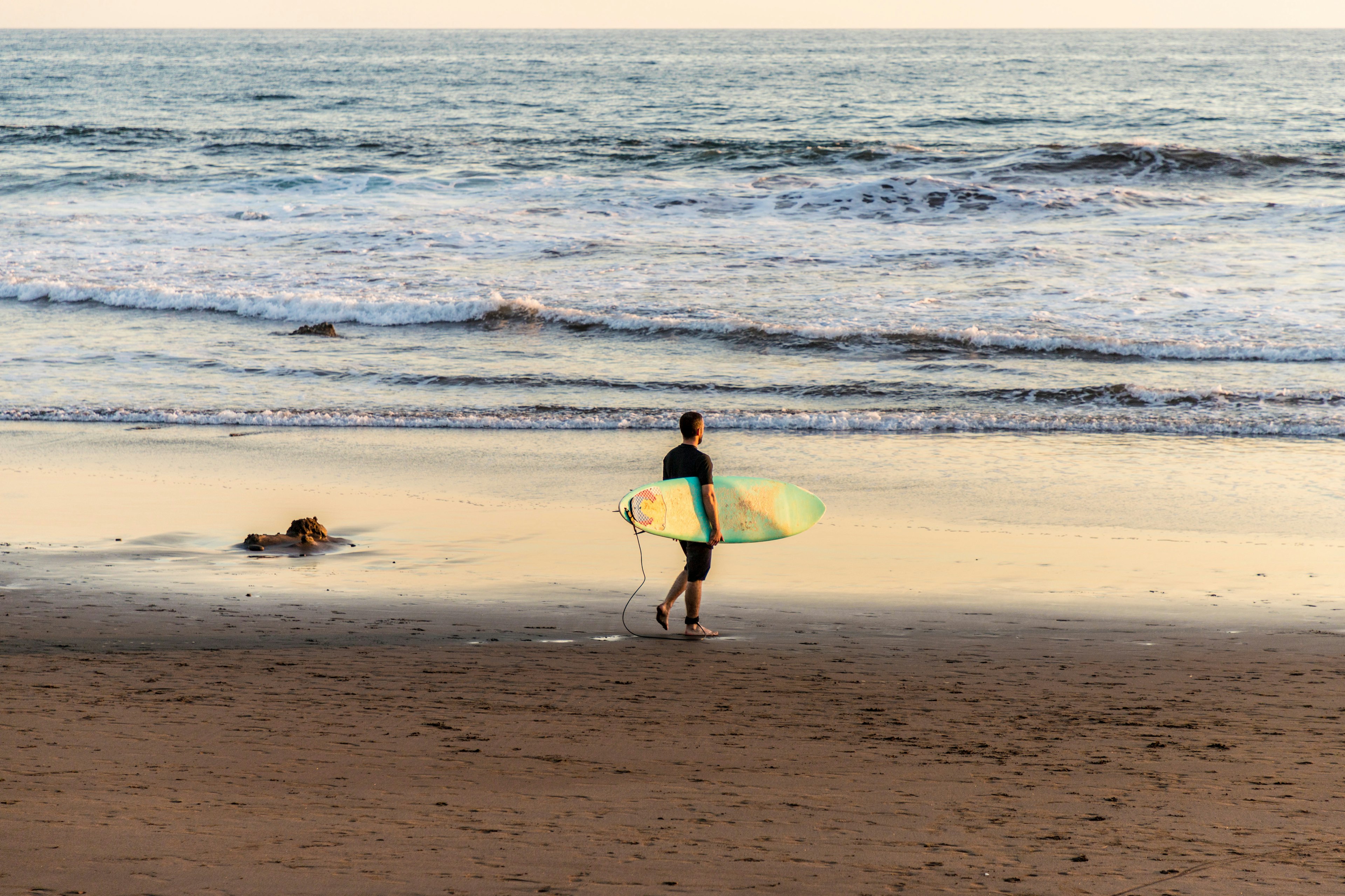 A surfer walking on the beach with his surfboard in Central America