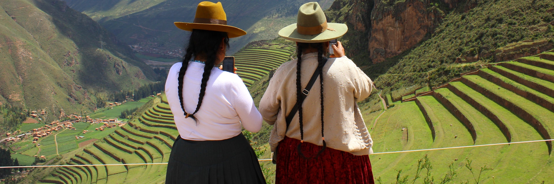 Two Peruvian woman look at their phones at the ancient ruins of Pisac.