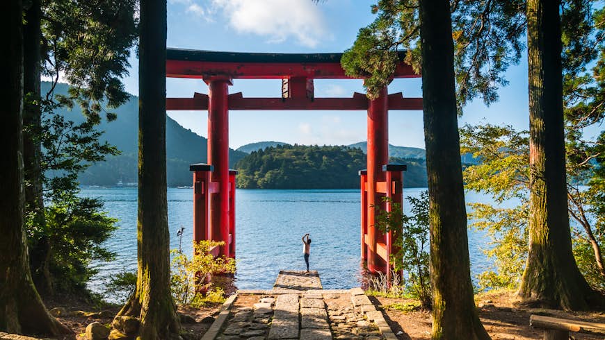 A young woman takes photos with her phone of a torii gate in Hakone, Japan