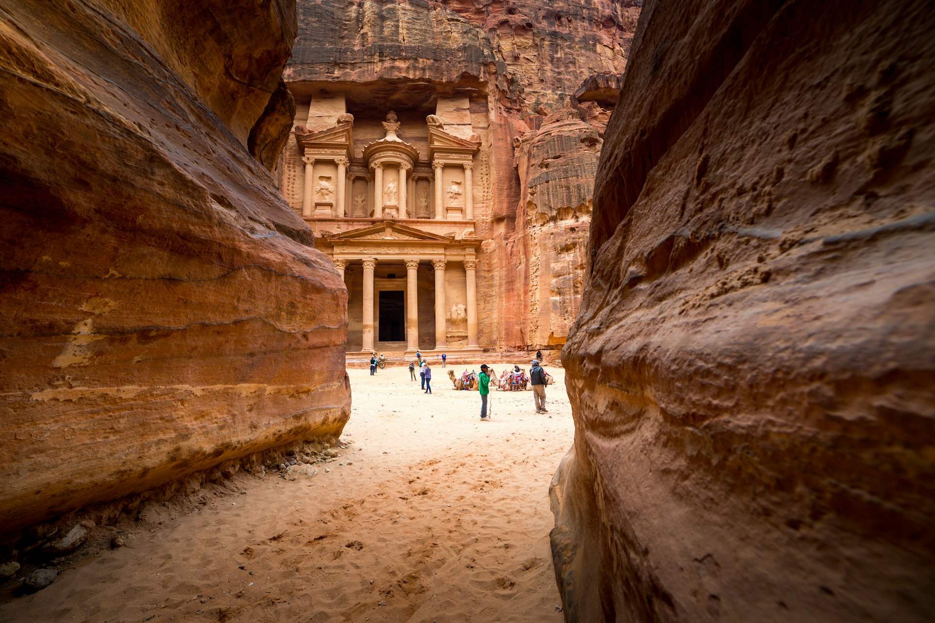 People in Al-Khazneh (The Treasury) in Petra, seen at the end of a sandy path through rocks  
