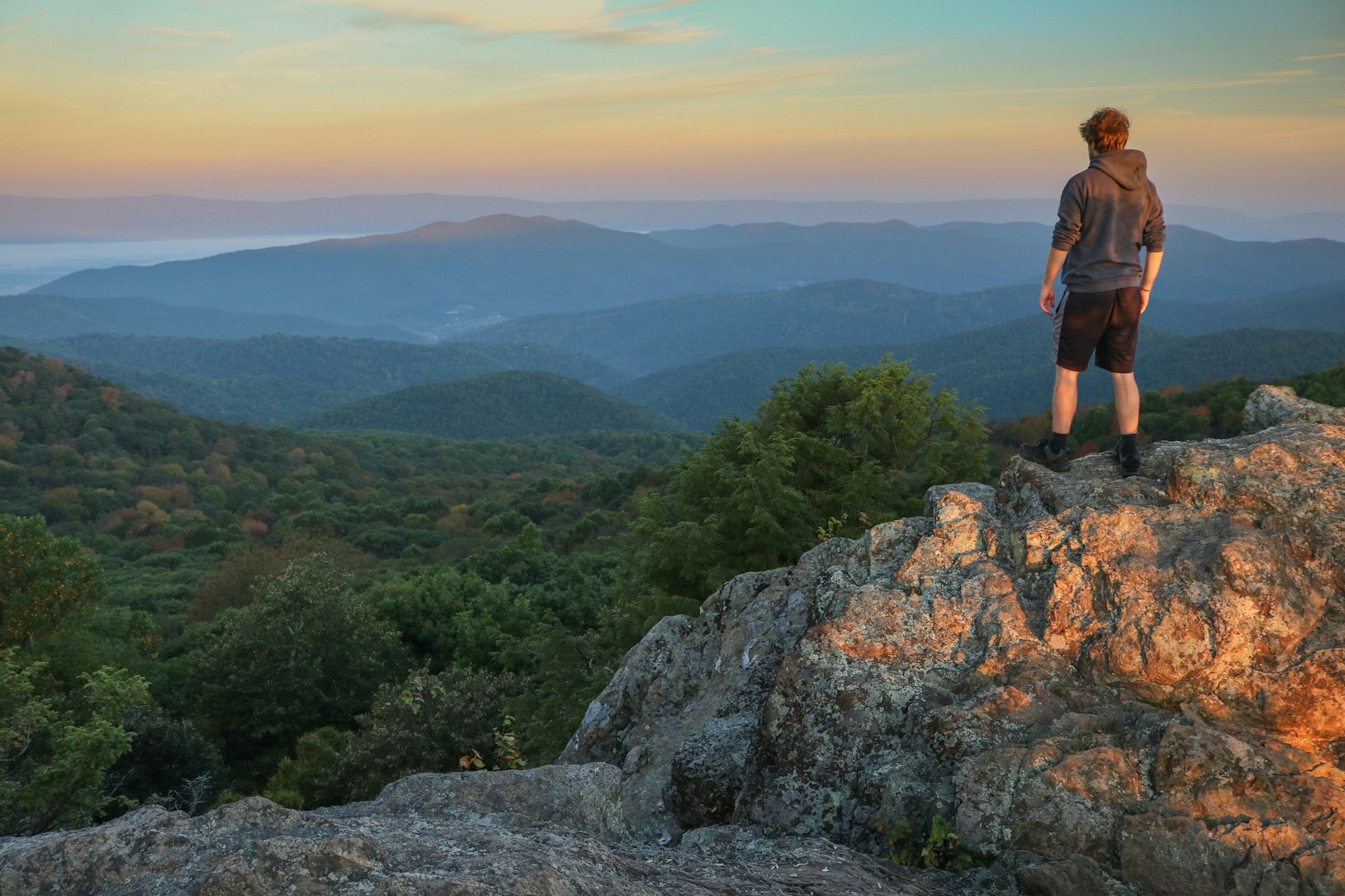 A male hiker stands on top of Bearfence Mountain at sunset in Shenandoah National Park