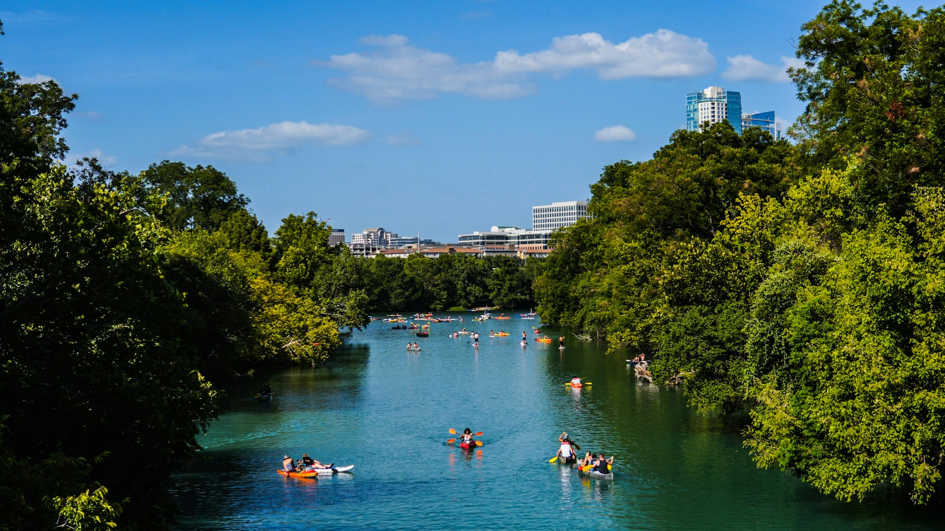 Multiple kayakers on Barton Creek in Austin, Texas with the city skyline in the distance