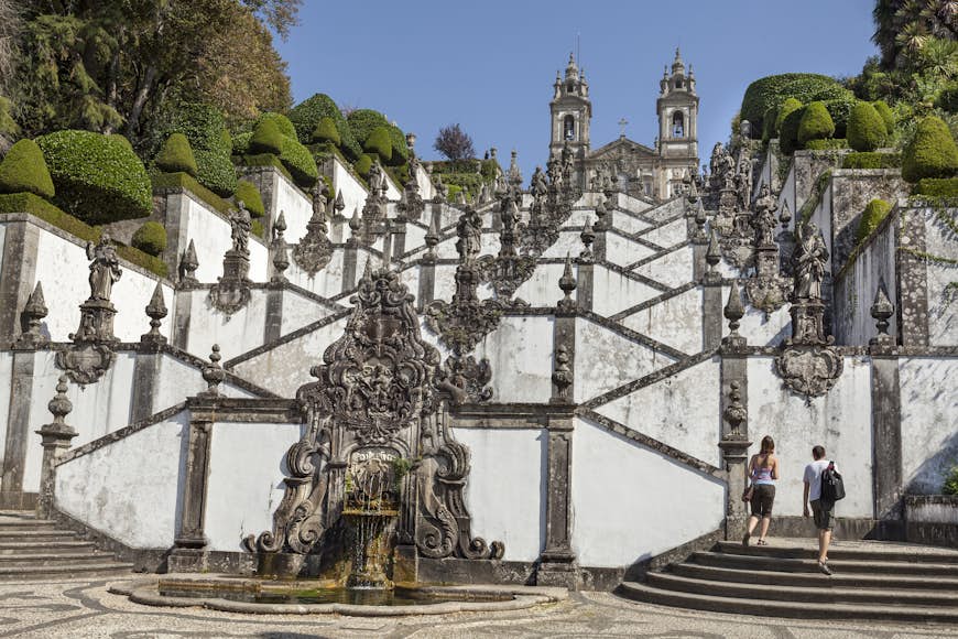 Tourists are approaching stairs with saint's statues leading to the church Bom Jesus do Monte near Braga, Portugal