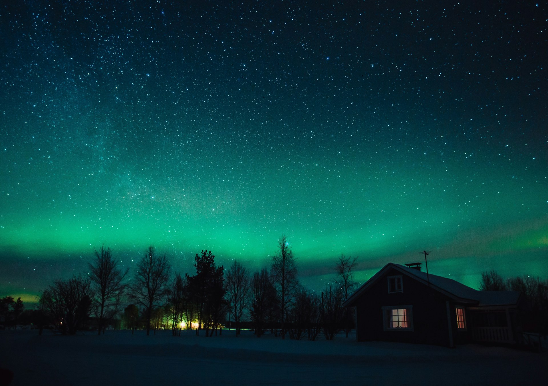 The Northern Lights (Aurora Borealis) over snowed-in cottage in Lapland village. Finland