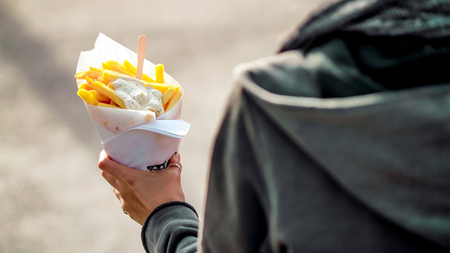 Brussels, Kingdom of Belgium. Tourist holds belgian fries in hand in the streets of Brussels. French Fries with mayonnaise.