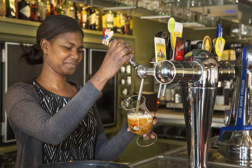 Black barmaid drawing Belgian draught beer in glass in Flemish tavern De Gulden Cop.