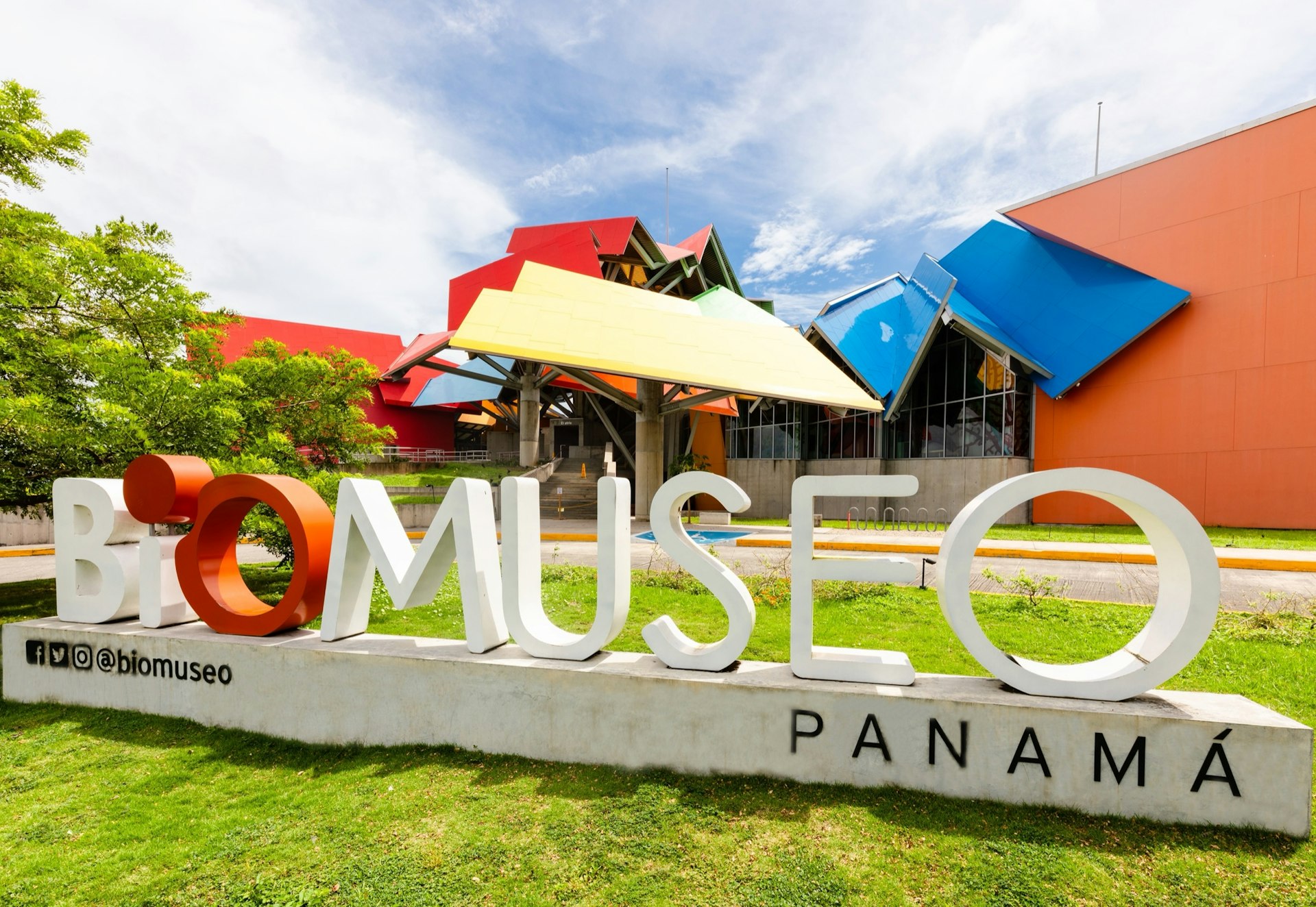 Exterior shot of the colorful BioMuseo in Panama. There is a BioMuseo sign on the grass. 