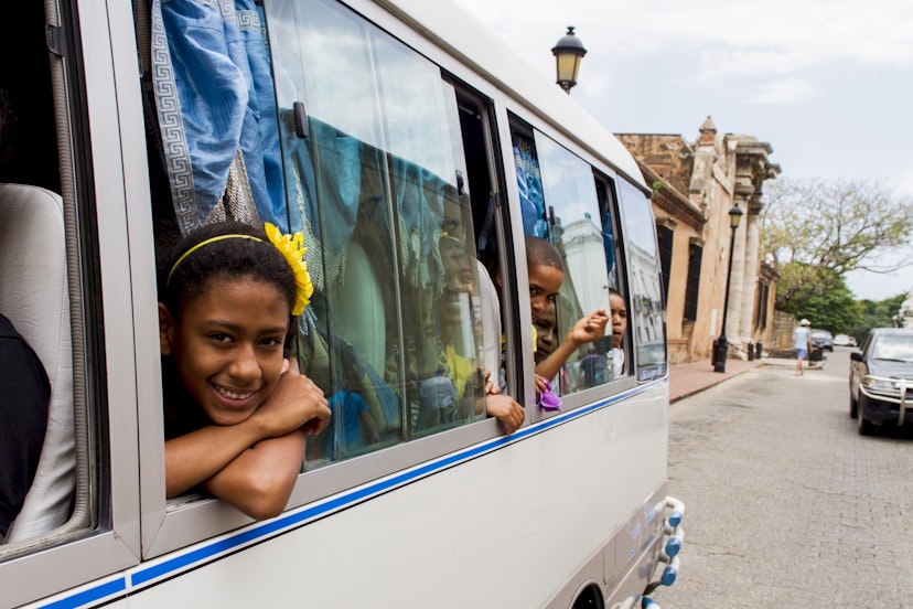 Children peek out of windows of a bus while traveling down a road in Santo Domingo, Dominican Republic. 