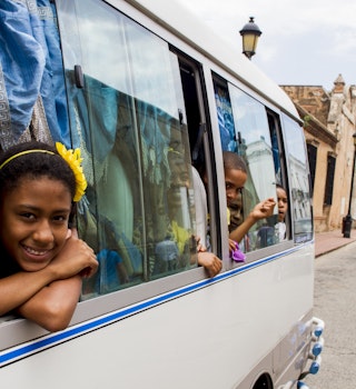 Children peek out of windows of a bus while traveling down a road in Santo Domingo, Dominican Republic. 