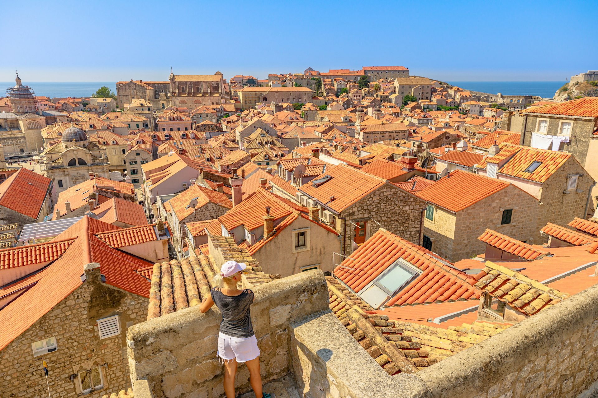 A woman seen from behind looking out onto the red-tiled roofs of an old town