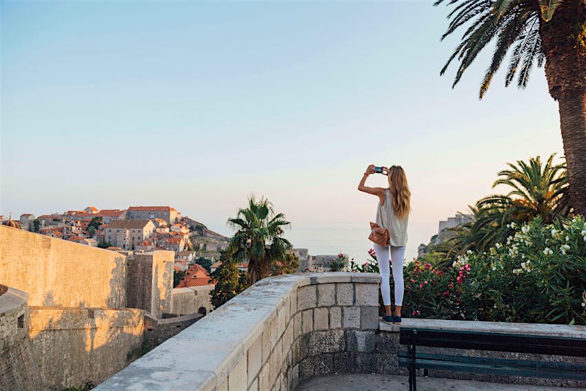 Caucasian woman standing on park wall photographing cityscape - stock photo