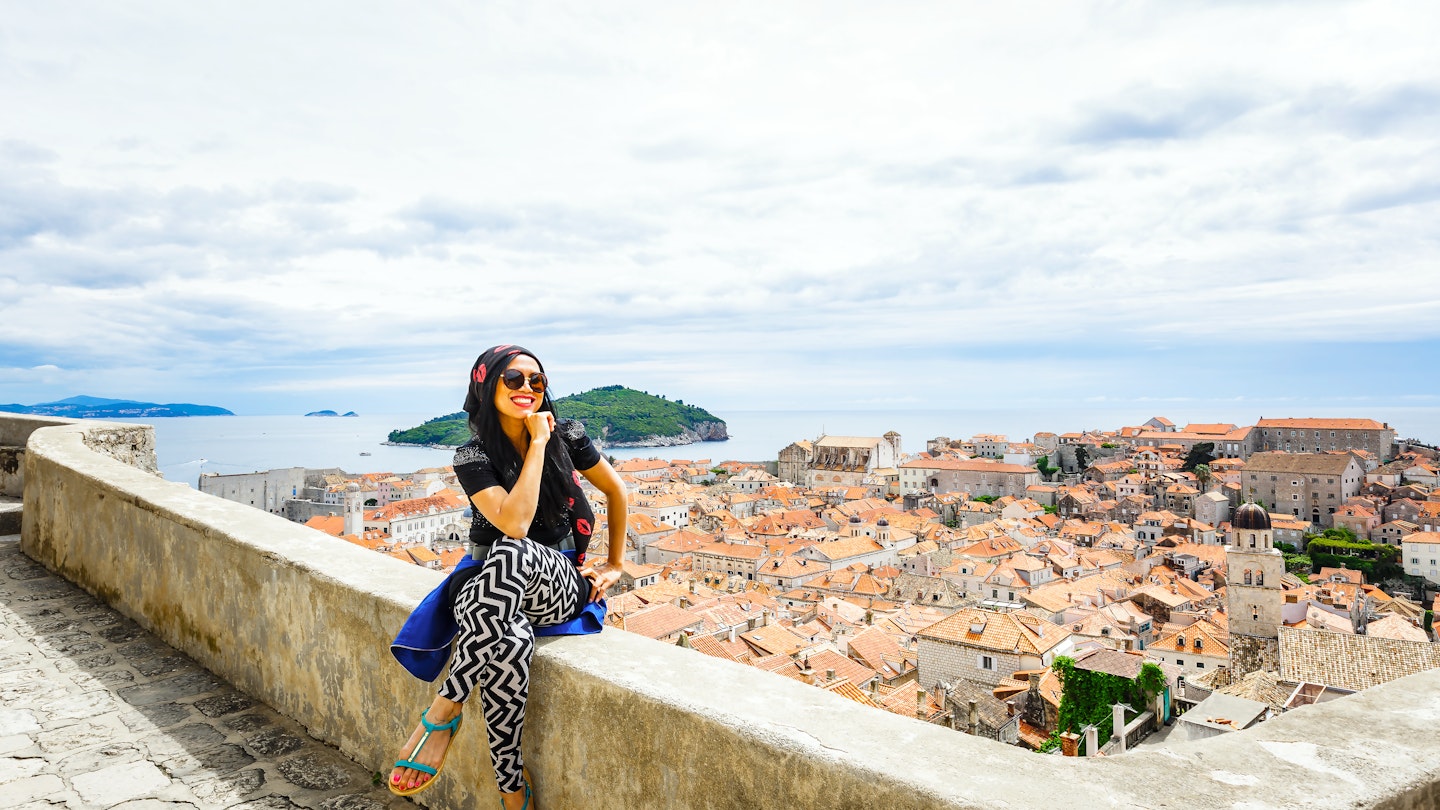 Happy smiling female tourist at Dubrovnik old city wall and old town by Adriatic sea of Croatia; Shutterstock ID 466118216; your: Claire Naylor; gl: 65050; netsuite: Online Ed; full: Dubrovnik neighborhoods
