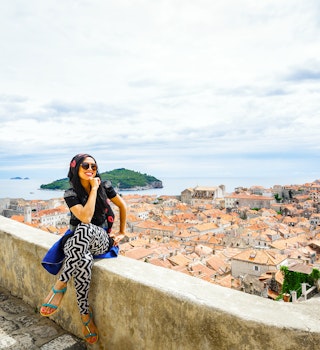 Happy smiling female tourist at Dubrovnik old city wall and old town by Adriatic sea of Croatia; Shutterstock ID 466118216; your: Claire Naylor; gl: 65050; netsuite: Online Ed; full: Dubrovnik neighborhoods