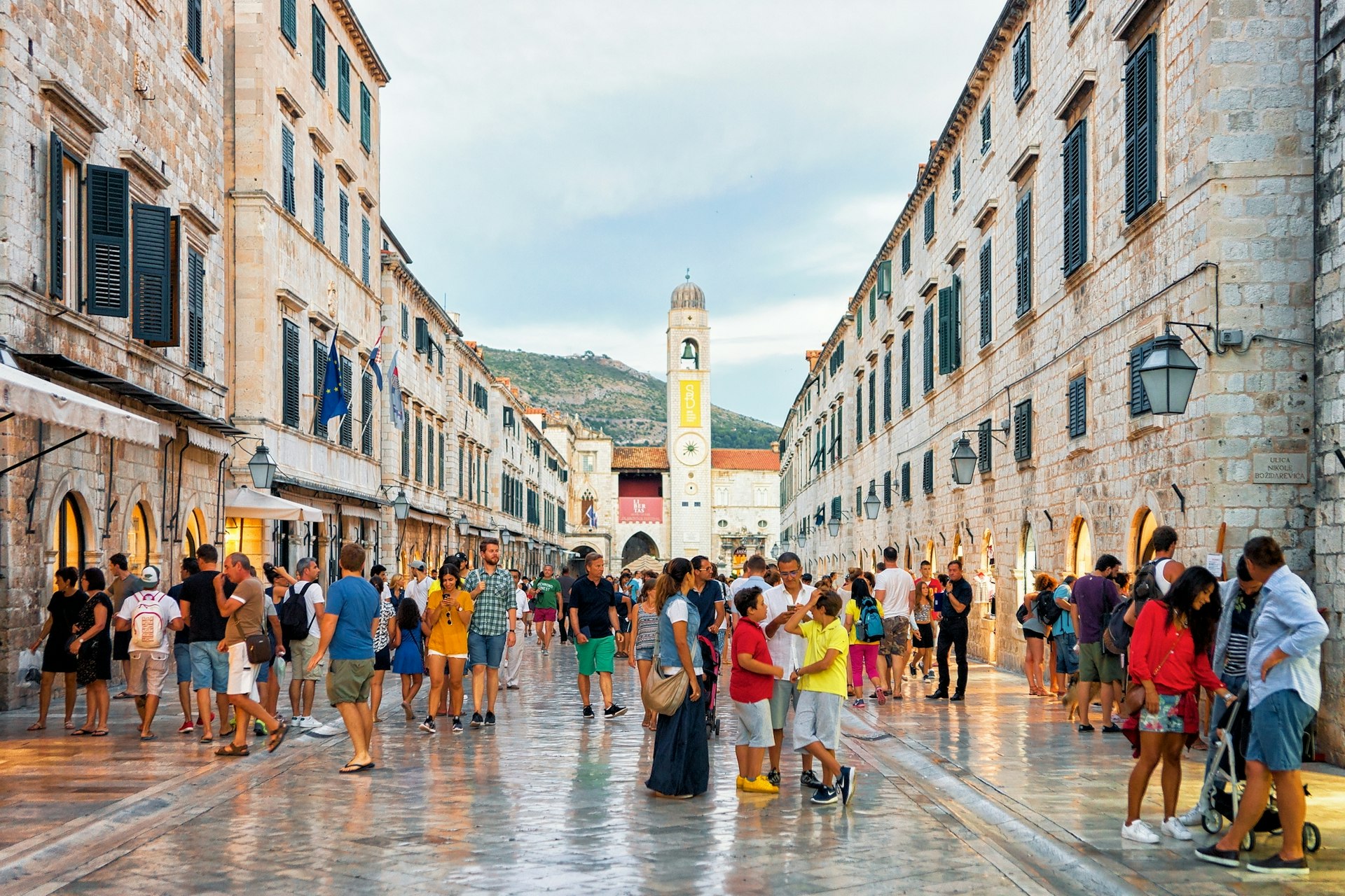 People in the old town of Dubrovnik on marble paths with a large bell tower in the distance