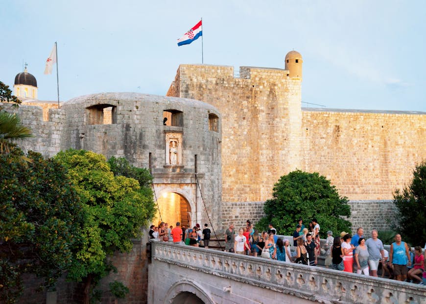 Les touristes traversent un pont vers une vaste passerelle en pierre dans les murs de la ville