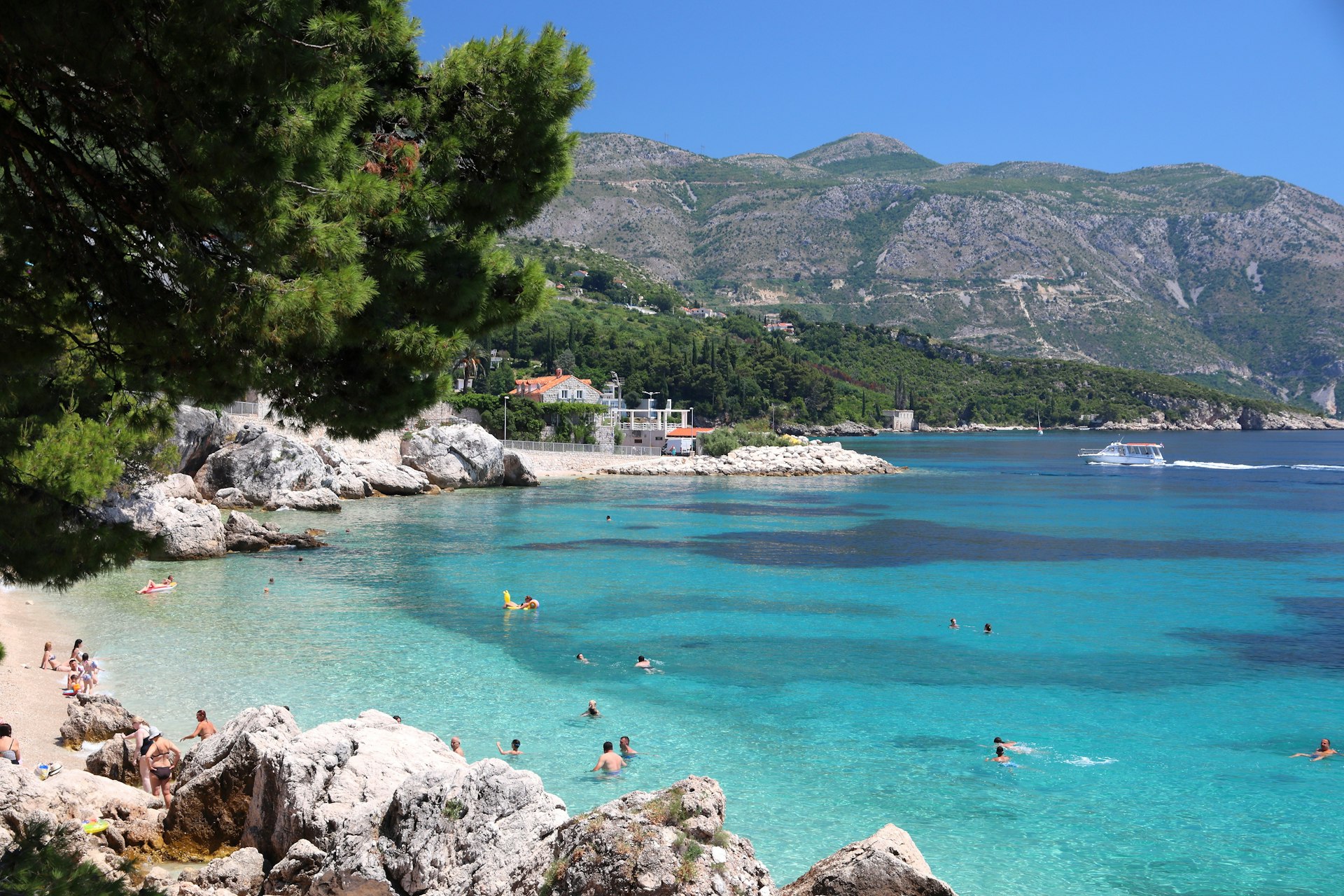 A turquoise sea with people swimming in it, with hills rising high above the sea in the distance