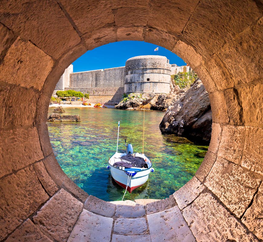 Le petit port de Dubrovnik avec un bateau soutenu par d'immenses murs de la ville vu à travers une fenêtre circulaire en pierre