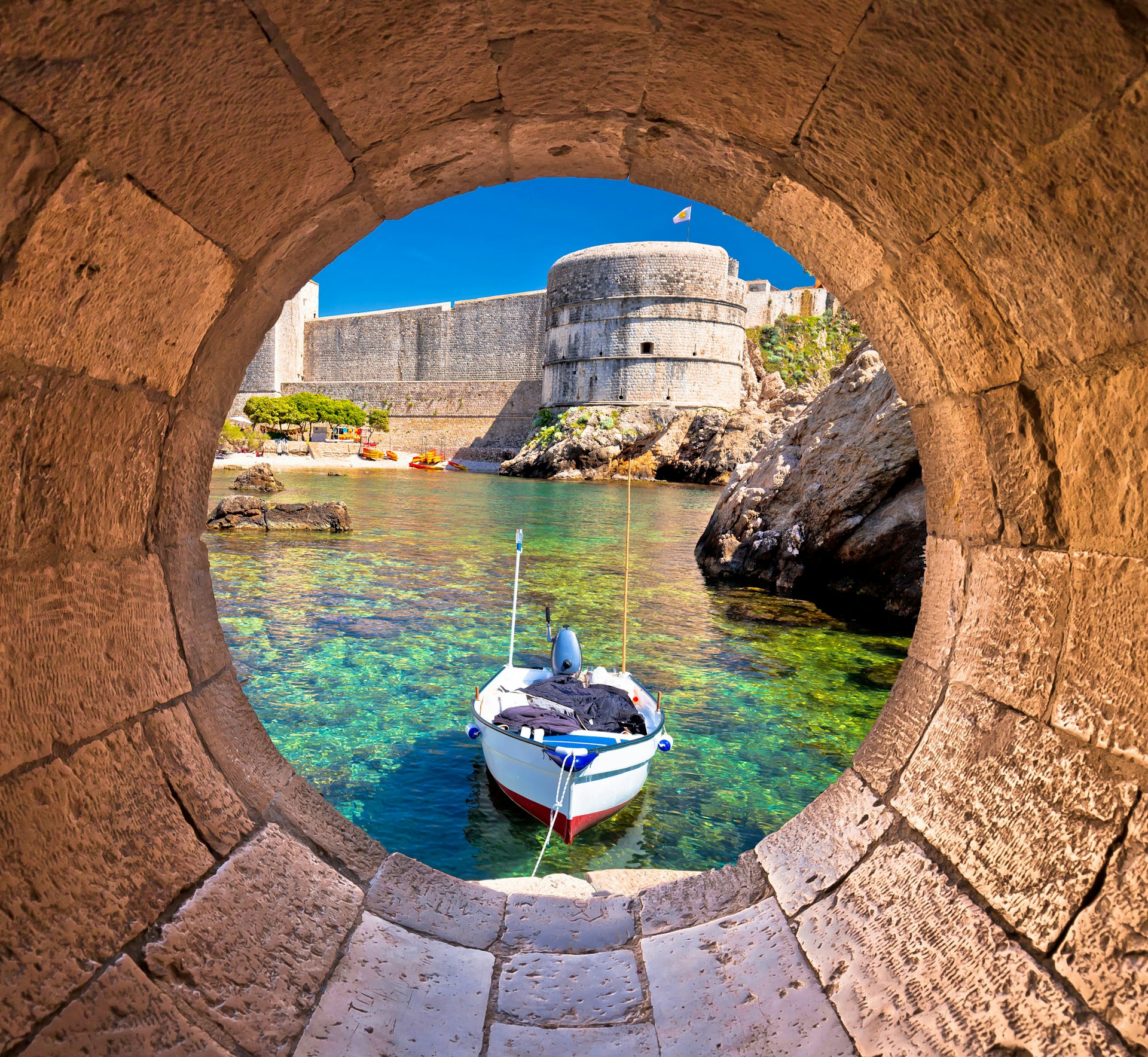 Dubrovnik's small harbor with a boat backed by huge city walls viewed through a stone circular window