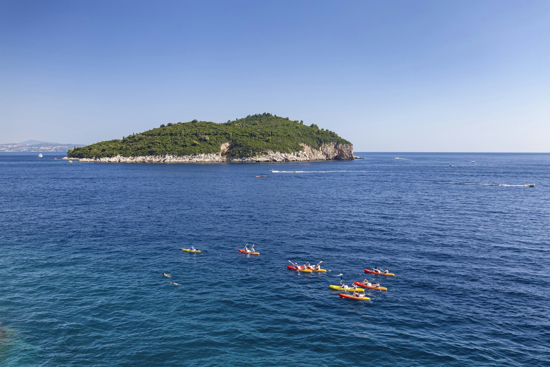 Yellow and red kayaks out at sea heading towards a forested island, Lokrum, off the coast of Dubrovnik