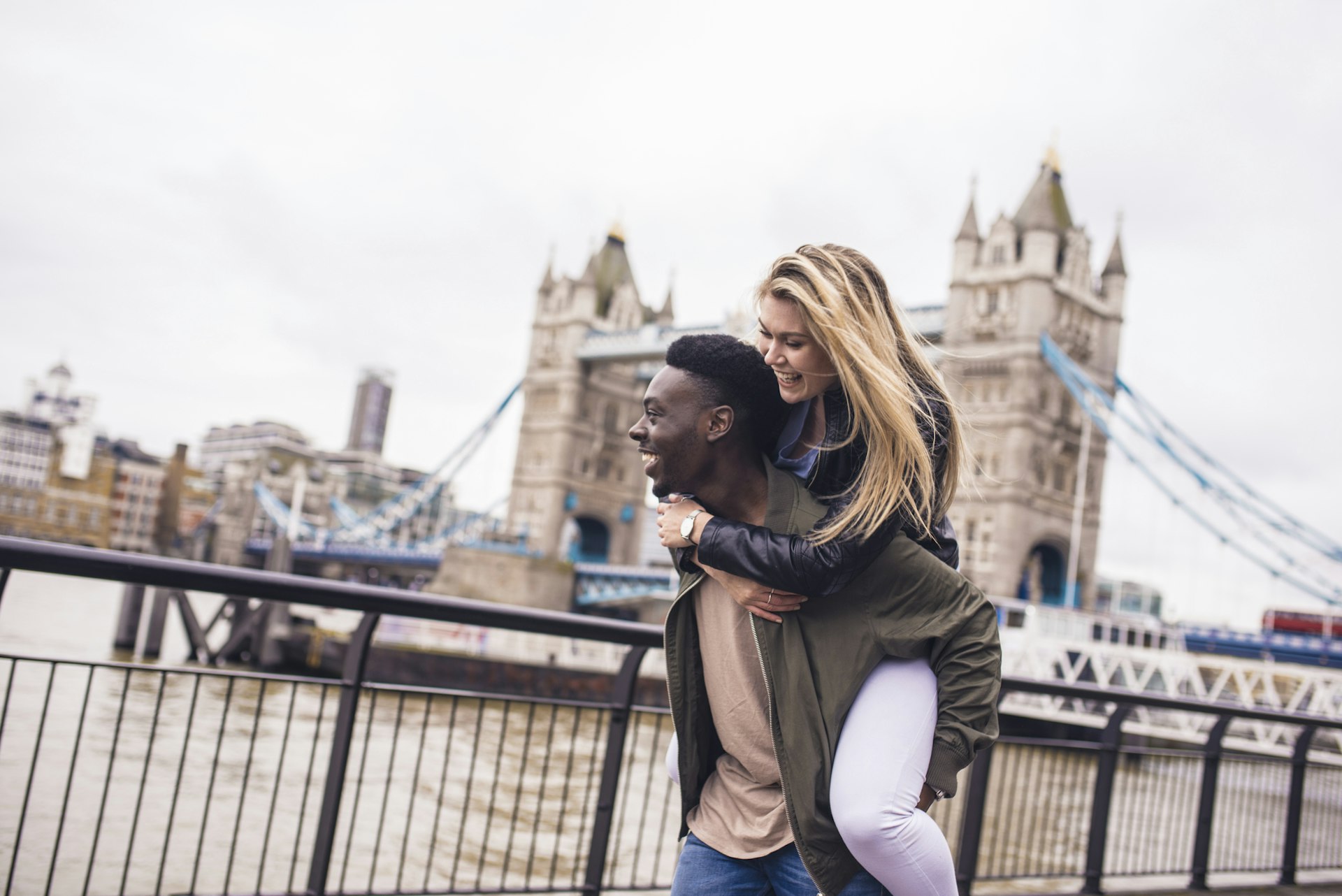 Two friends walk the streets of London with Tower Bridge behind them