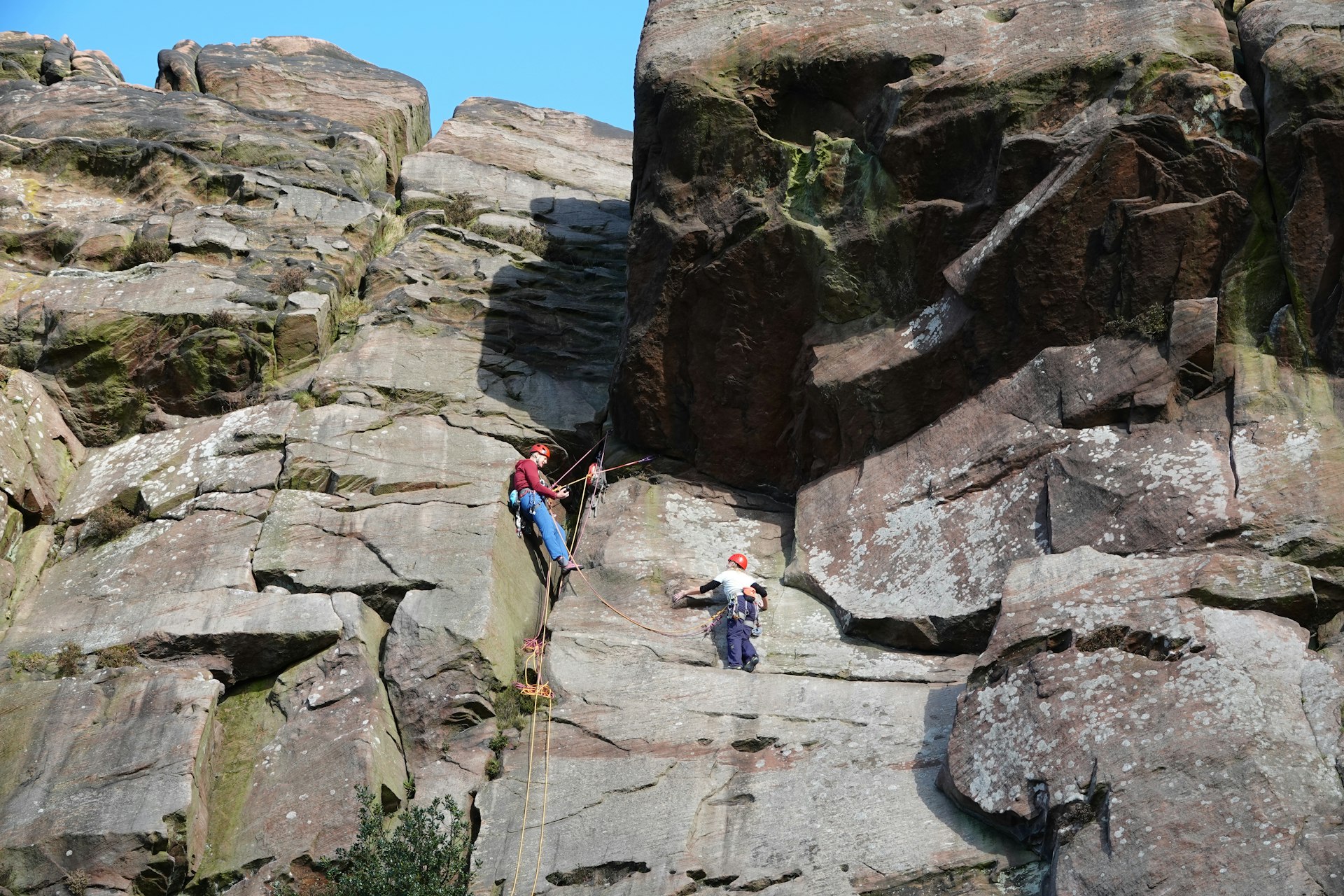 Two climbers on ropes at the face of a large rock in the Peak District National Park