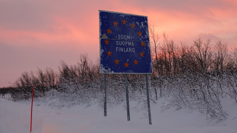 Rugged wintry wilderness surrounds the blue border crossing traffic sign at sunset. Snow covering the bushes under the large traffic sign In the rugged Finnish countryside on a sunny winter evening.; Shutterstock ID 1214054785; your: Brian Healy; gl: 65050; netsuite: Lonely Planet Online Editorial; full: Do you need a visa for Finland?